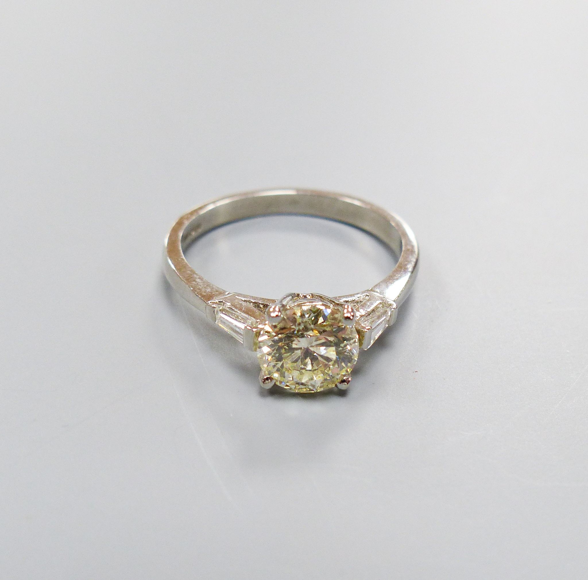 A modern platinum and single stone diamond ring, with trapeze cut diamond set shoulders, size O, gross weight 4.3 grams